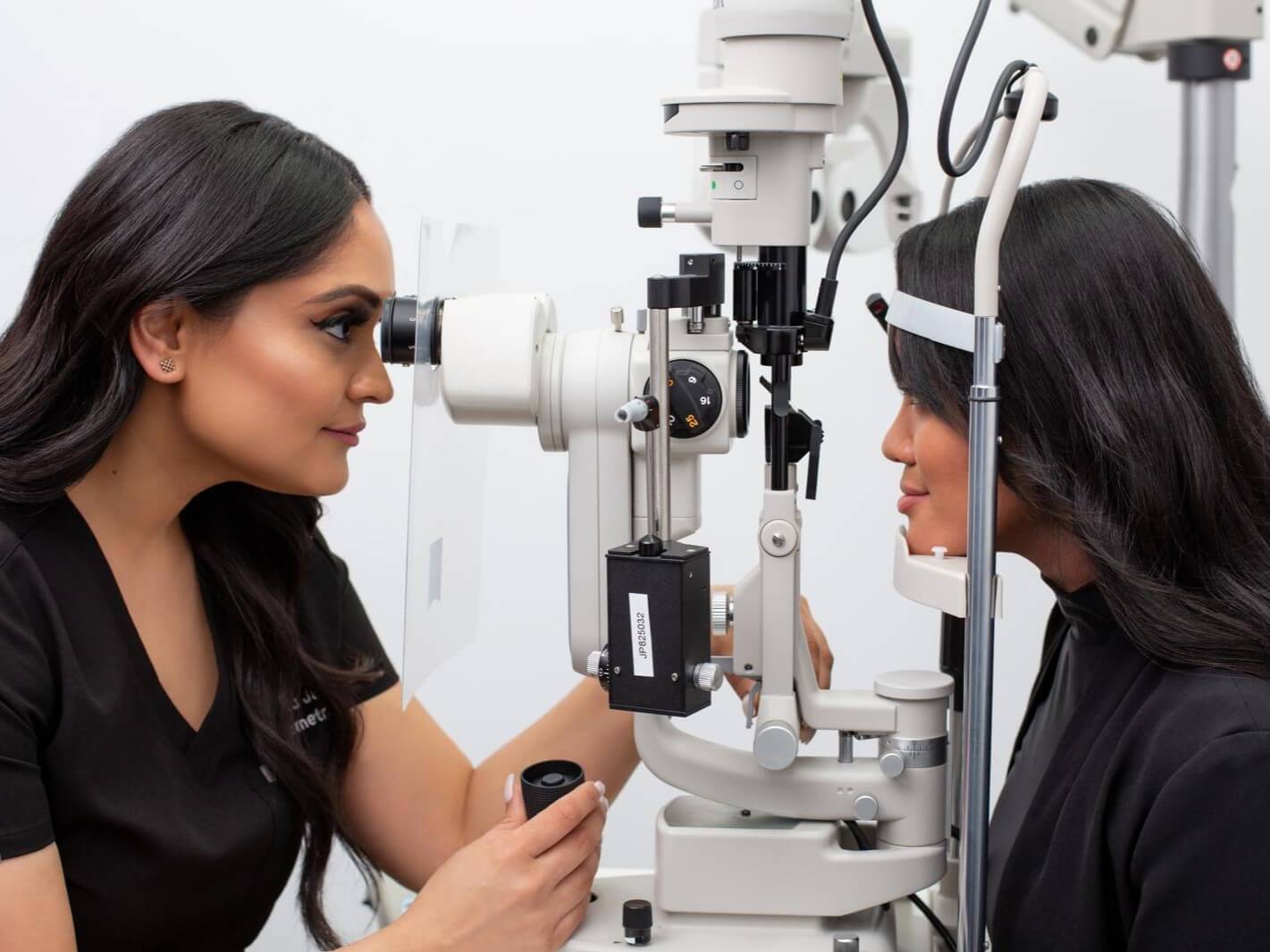Two women using an eye examination machine in a clinical setting